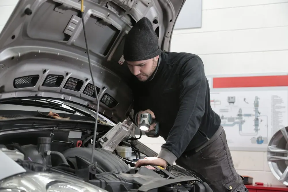 Szakember lámpával vizsgálja egy autó motorterét